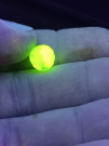 Korálek z uranového skla svítící v UV světle.